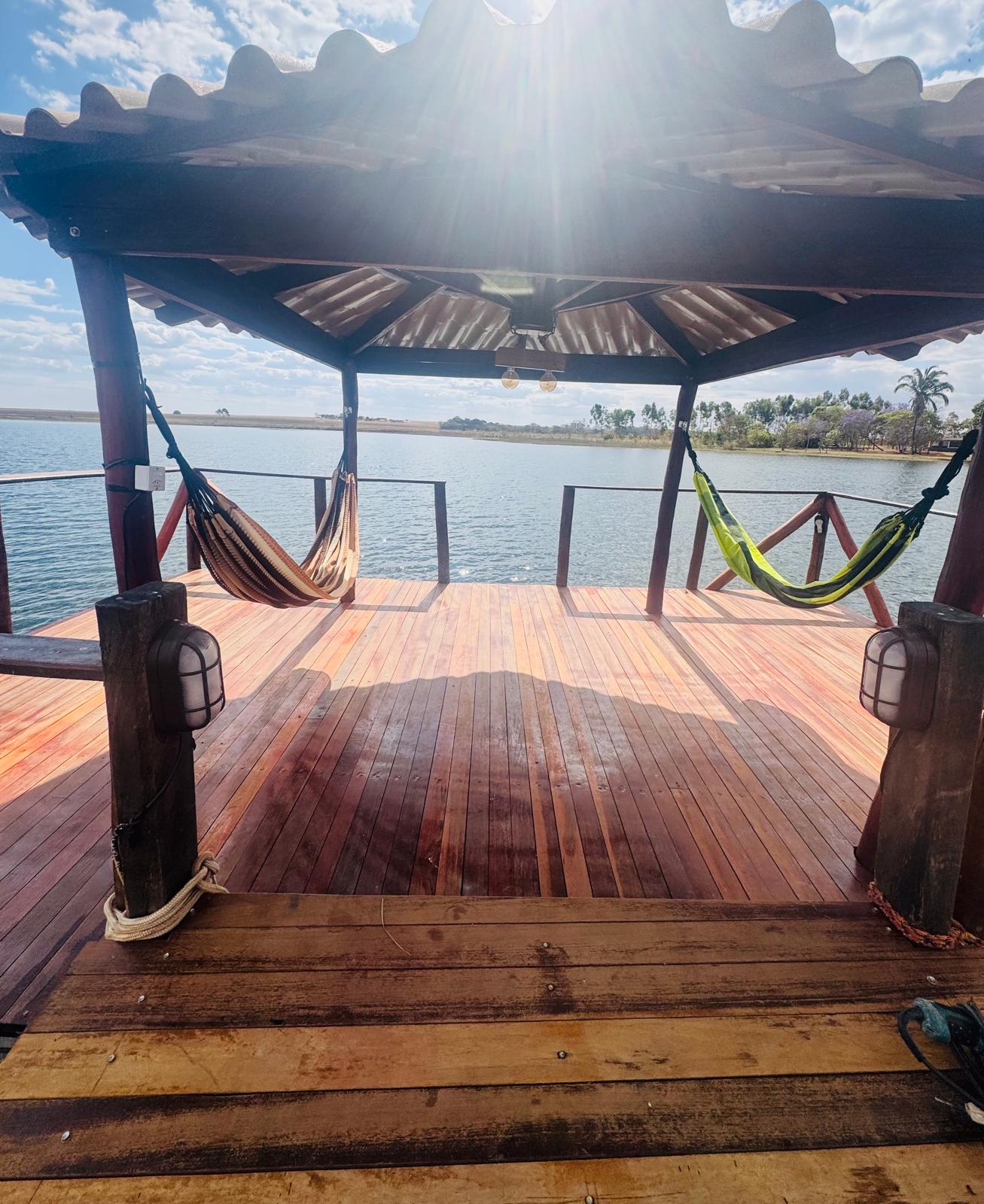 Interior do quiosque de madeira sobre a represa no final do píer, com redes de descanso e piso de deck envernizado