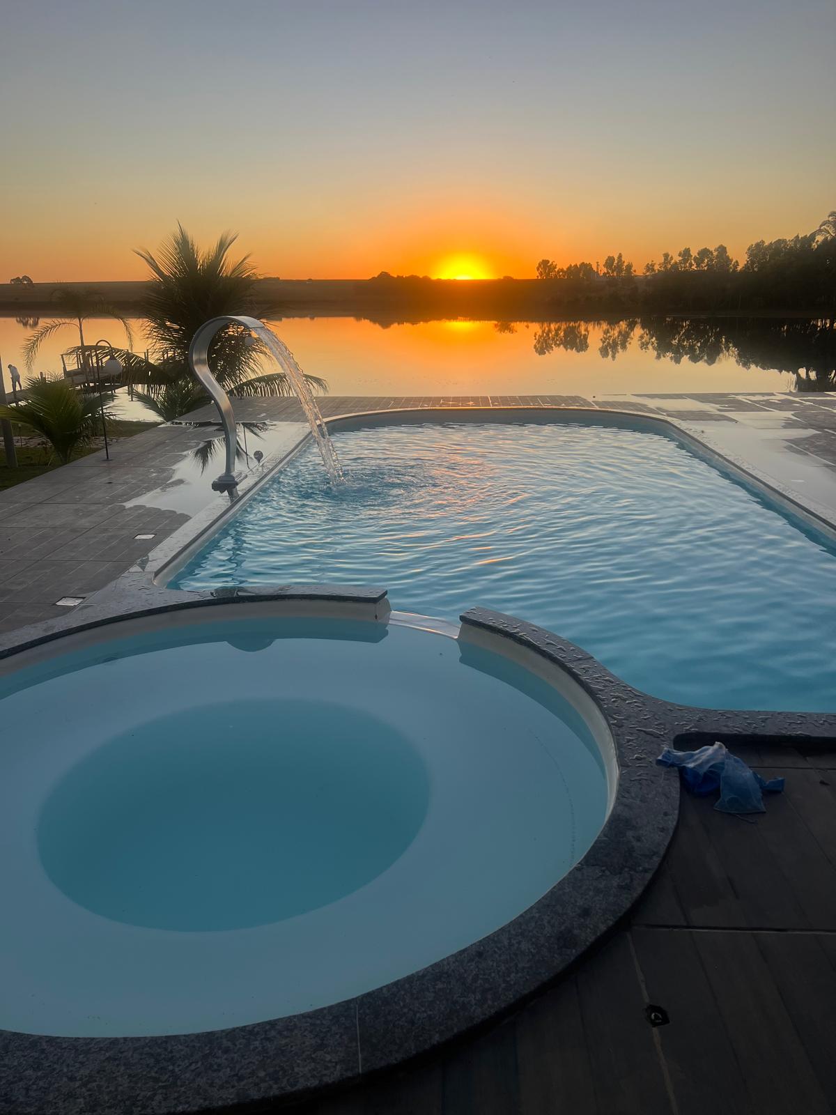 Piscina privativa com cascata inox tipo bico de pato e hidromassagem redonda acoplada, de frente para o pôr do sol na represa